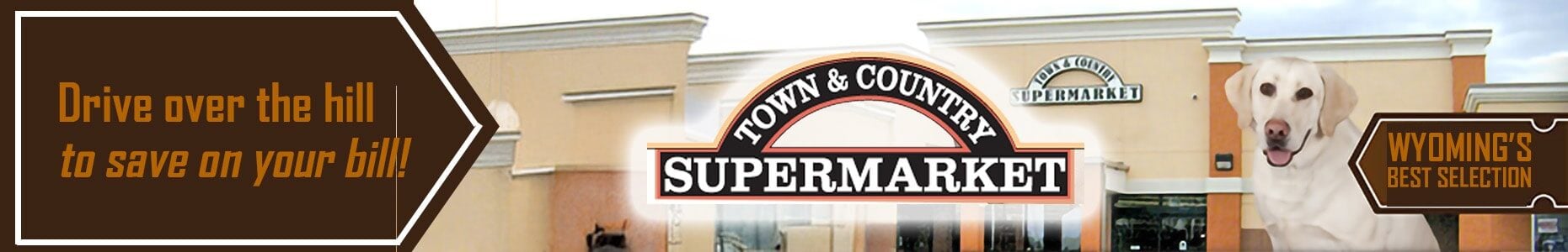Town & Country Supermarket storefront with a slogan reading "Drive over the hill to save on your bill!" and a white Labrador dog promoting Wyoming’s best selection.